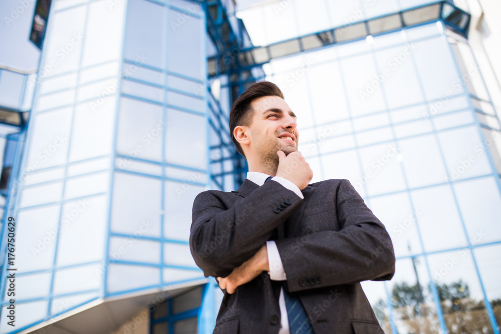 Thinking about solutions. Side view of young man in formalwear holding hand on chin and looking away while standing outdoors