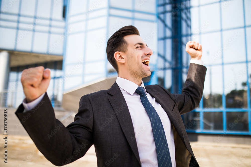 Handsome businessman raising arms in sign of victory outdoors against office building Handsome businessman raising arms in sign of victory outdoors against office building
