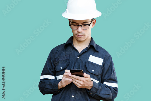 Asian man,Engineer or Technician in white helmet, glasses and blue working shirt suit using smart phone, isolated on green, mechanic and Oil and Gas industrial concept with clipping path