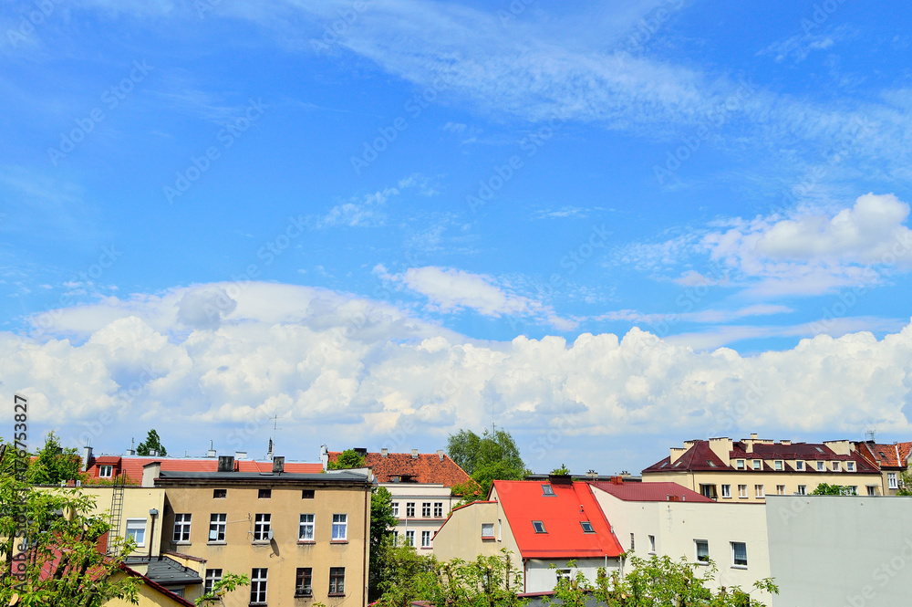 Niebieskie niebo i białe chmury nad dachami budynków mieszkalnych.