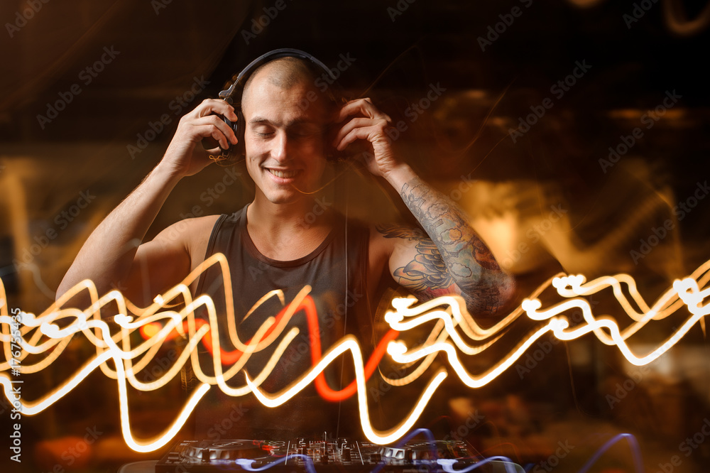 Obraz premium Smiling DJ in headphones on the background of night club lights