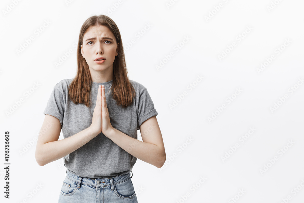 Fototapeta premium Please, forgive me. Young beautiful european girl with dark healthy hair and brown eyes in grey clothes looking in casmera with guilty expression, trying to ask for forgiveness from mother.