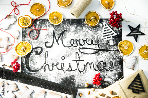 inscription Christmas on a black board sprinkled with flour among the Christmas decor, ginger biscuits and dried oranges
