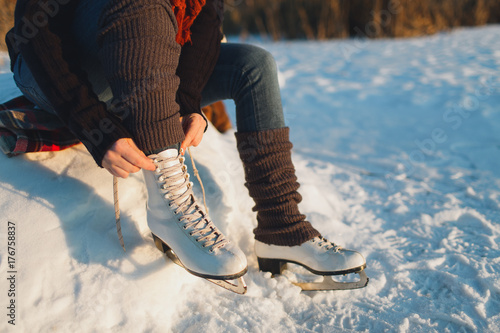 Cropped image of a woman putting ice skates on. Woman lacing ice skates at the edge of a frozen lake. photo