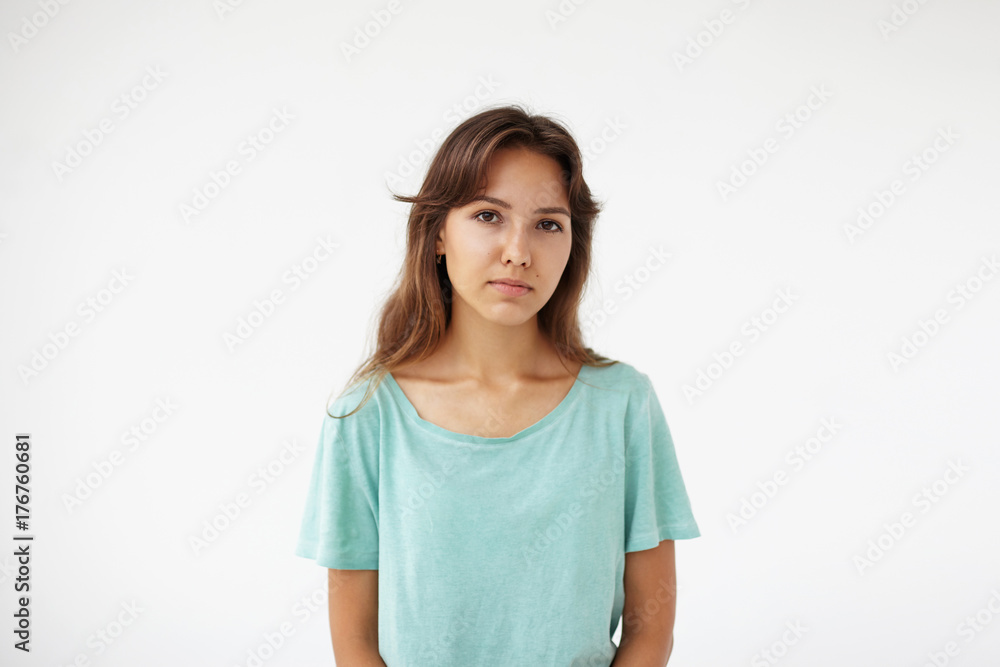Youth and skin care concept. Cropped portrait of beautiful charming young Hispanic female with brown eyes, clean skin and dark hair posing at white studio wall, having calm or serious expression Youth and skin care concept. Cropped portrait of beautiful charming young Hispanic female with brown eyes, clean skin and dark hair posing at white studio wall, having calm or serious expression
