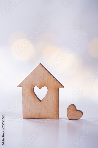 Wooden house with hole in the form of heart with little heart on light bokeh background