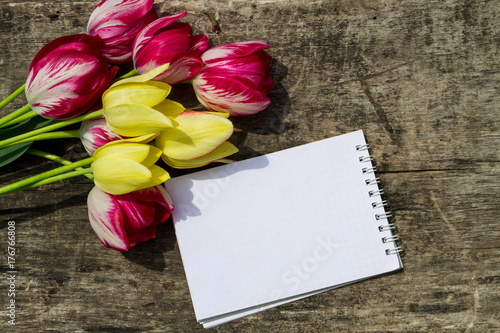 Bouquet of tulip flowers and blank notepad on rustic wooden background