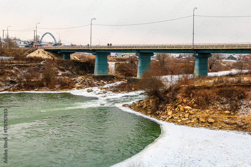 Car bridge over the ice-free river. Boiling water, river rapids, snow on the banks