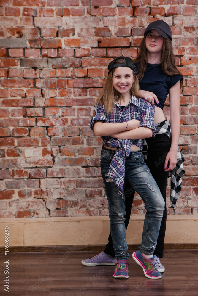 Urban style. Friendship in hip hop. Stylish female teenagers in studio, happiness in dance, brick wall background with free space. Happy street life, beautiful sisters concept