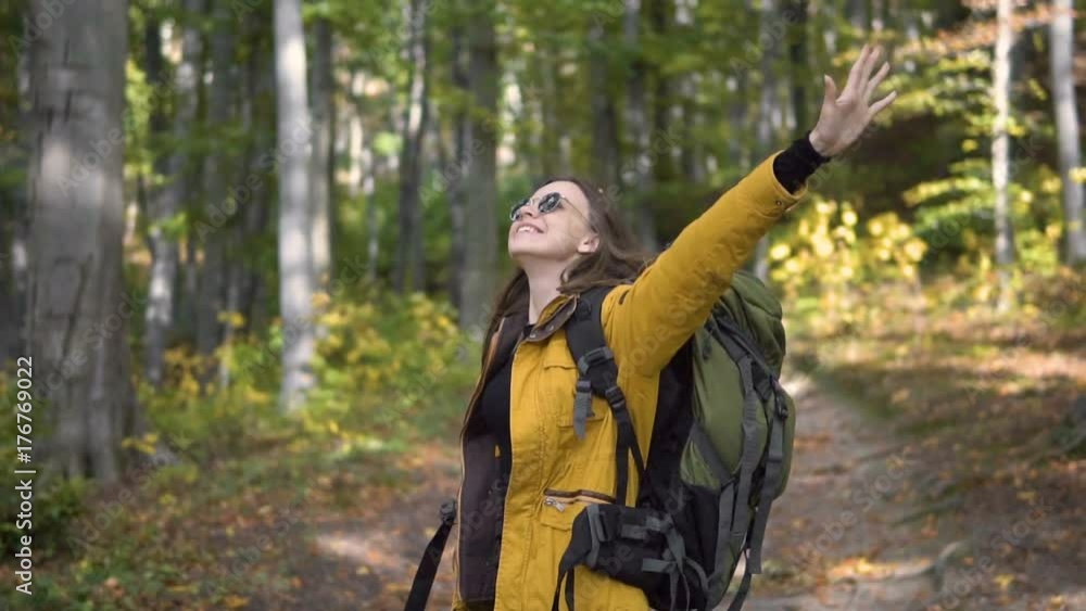 Caucasian female tourist, in yellow jacket and black sunglasses, enjoys the fall forest with arms wide open, slowmotion Caucasian female tourist, in yellow jacket and black sunglasses, enjoys the fall forest with arms wide open, slowmotion