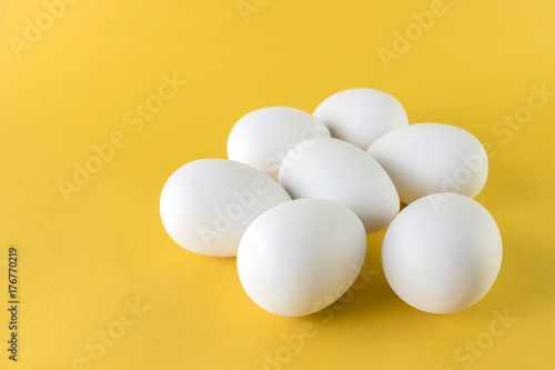 Seven white hen eggs isolated on yellow background
