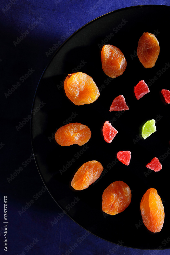 Dried apricots, candied fruits in sugar on a black plate on a dark blue background Dried apricots, candied fruits in sugar on a black plate on a dark blue background