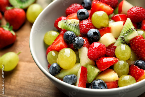 Bowl with yummy fruit salad on wooden board