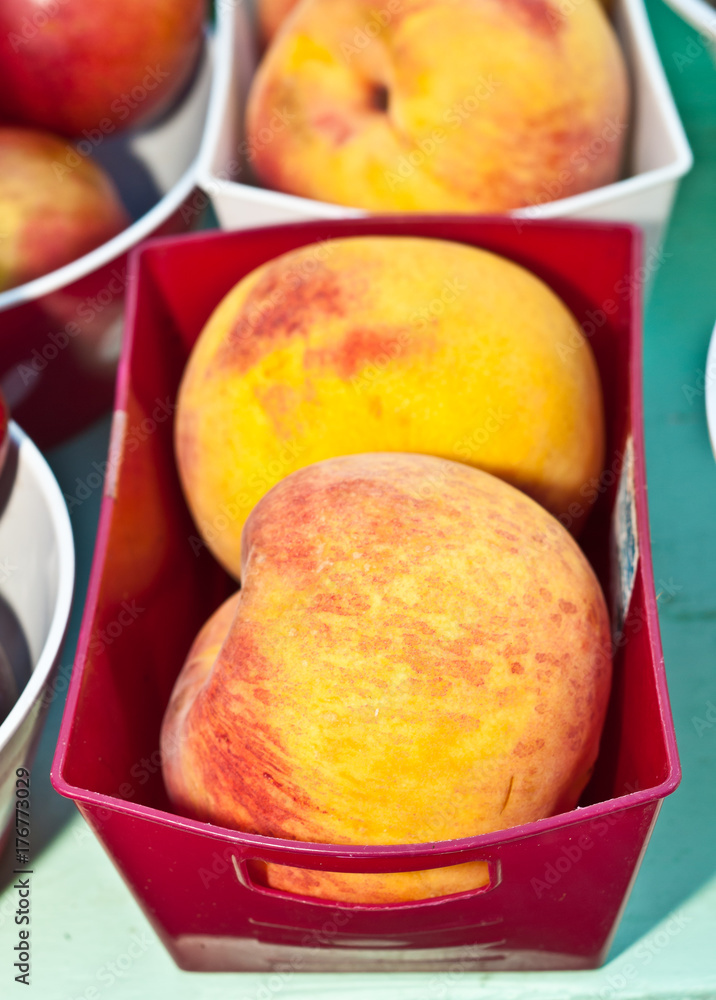 Local, ripe, organic, just picked peaches in a red, plastic container, for sale at an autumn farmers market