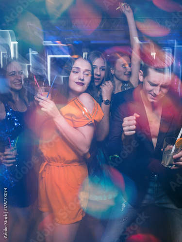 Happy friends dance in motion. Joyful New Year company in night club, active Christmas celebration. Disco party in blurred colors, modern youth life