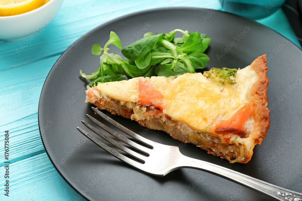 Plate with piece of salmon quiche pie on table, closeup