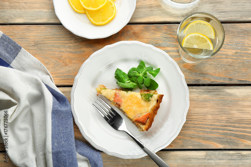 Plate with piece of salmon quiche pie on table