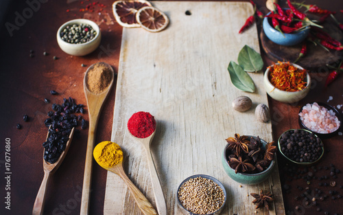 Various indian spices in wooden spoons, seeds, herbs and nuts and empty wooden board