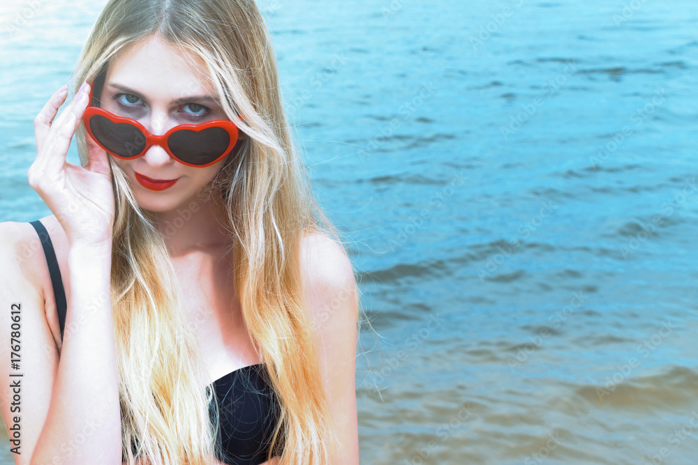 Portrait of attractive young woman with long hair against blue sky. Girl posing on sunny beach. Vintage style