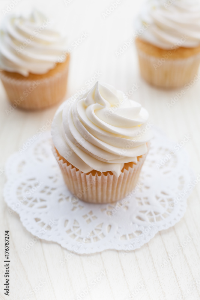Vanilla cupcakes topped with swirl of sweet vanilla frosting captured on the wooden table in a sunny day. Vanilla cupcakes topped with swirl of sweet vanilla frosting captured on the wooden table in a sunny day.