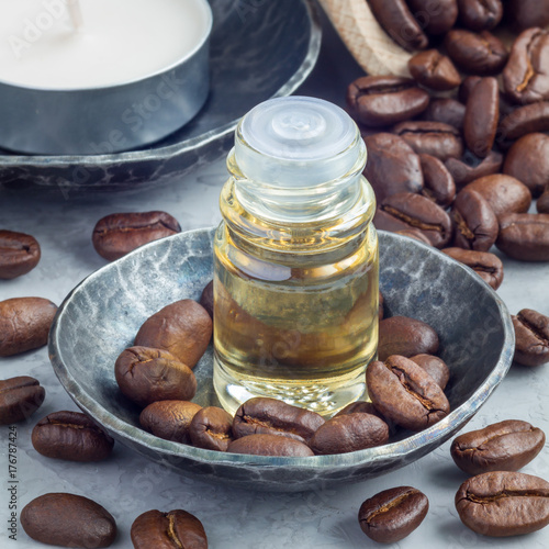 Coffee essential oil in glass bottle on background with coffee beans, square format