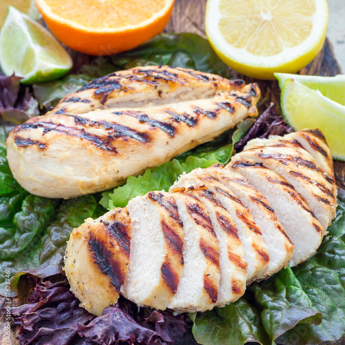 Grilled chicken breast in citrus marinade on salad leaves and wooden cutting board, square format