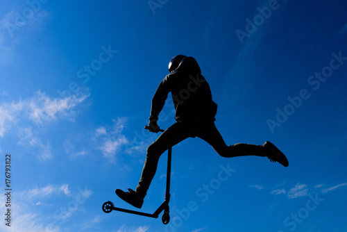 The teenager on the scooter in a jump against the background of the sky. Backlight. photo