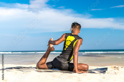 Asian yoga man practice yoga on the beach with a clear blue sky background. Yogi on the tropical beach of Bali island, Indonesia.