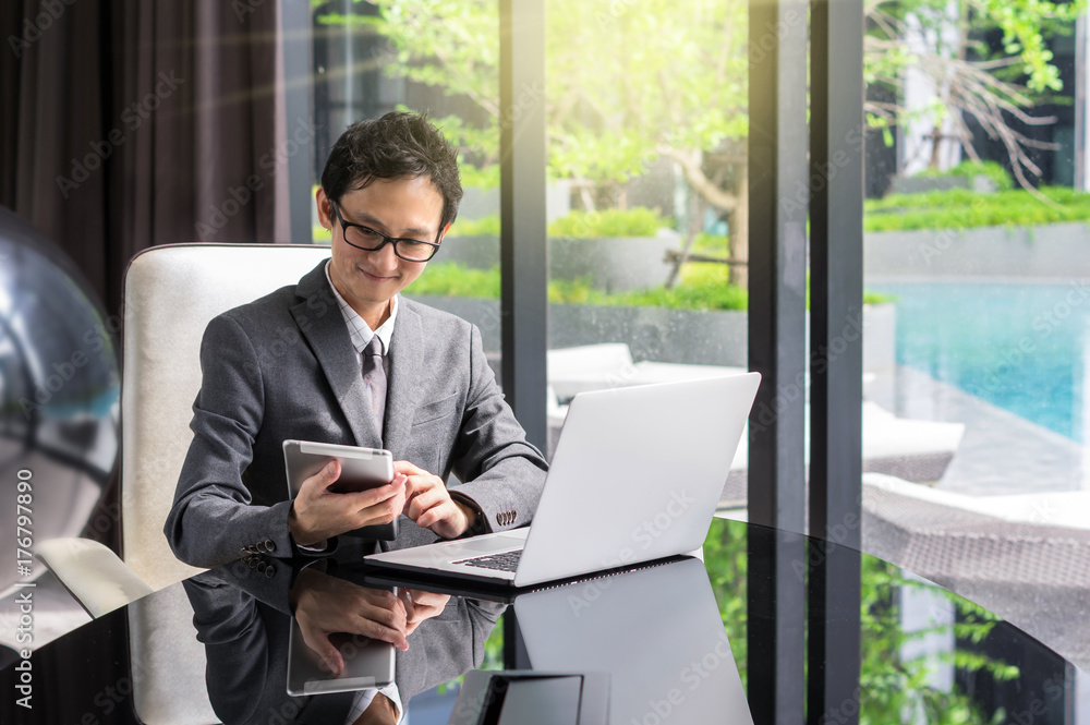 Happy young asian businessman sitting on working space and using laptop and tablet. business communication concept Happy young asian businessman sitting on working space and using laptop and tablet. business communication concept