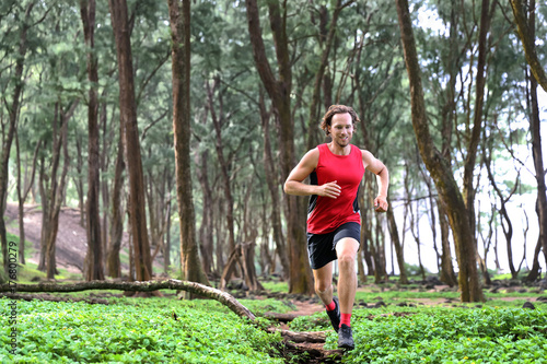 Trail runner man athlete running through forest nature on path sprinting jumping over wood. Sport sprinter active doing high intensity training outdoors in summer landscape.