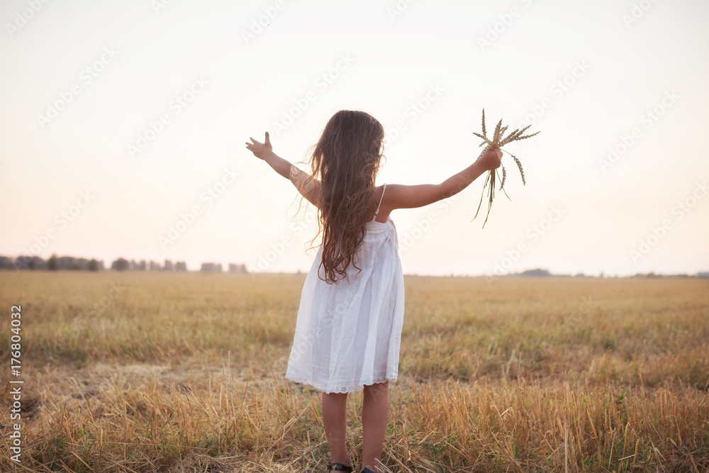 Little beautiful smiling girl on a gold wheat field walking at sunset. Happy five years old girl smiling and laughing in summer day at nature. Happyness freedom and carefree childhood concept Little beautiful smiling girl on a gold wheat field walking at sunset. Happy five years old girl smiling and laughing in summer day at nature. Happyness freedom and carefree childhood concept