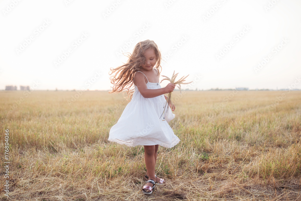 Little beautiful smiling girl on a gold wheat field walking at sunset. Happy five years old girl smiling and laughing in summer day at nature. Happyness freedom and carefree childhood concept Little beautiful smiling girl on a gold wheat field walking at sunset. Happy five years old girl smiling and laughing in summer day at nature. Happyness freedom and carefree childhood concept