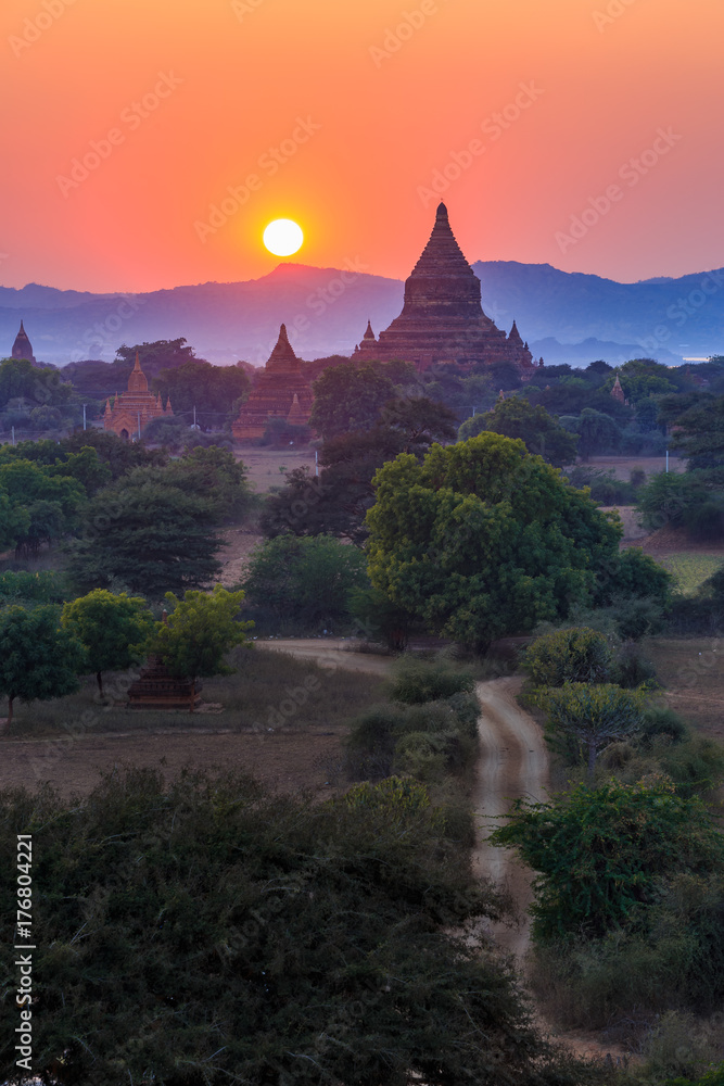 View from afar of the ancient pagodas (stupas) visible among rugged fields and trees of other pagodas and mountains on the horizon during sunset or sunrise, in Bagan, Myanmar (Burma) View from afar of the ancient pagodas (stupas) visible among rugged fields and trees of other pagodas and mountains on the horizon during sunset or sunrise, in Bagan, Myanmar (Burma)