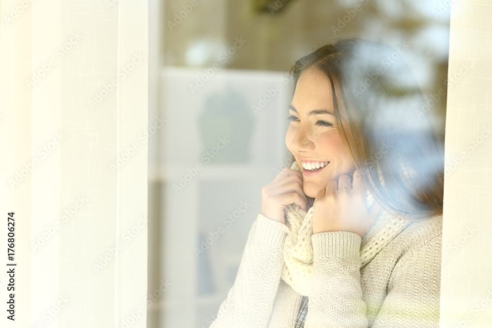 Happy woman looking through a window in winter