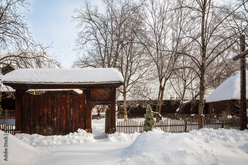 Traditional wooden gate and a homestead in a winter setting at the Village Museum in Bucharest, Romania.