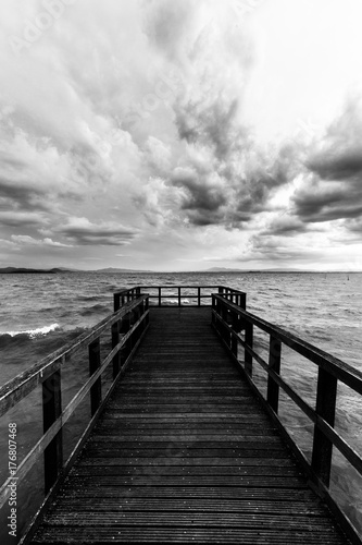 First person view of a pier on a lake on a moody day, with dark water and overcast, stormy sky