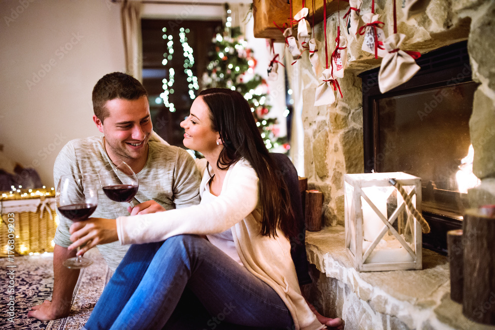Couple sitting in front of fireplace, drinking wine.