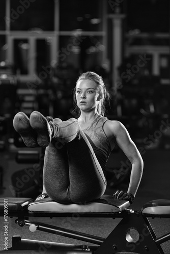 Woman doing strength exercises for abdominal muscles at indoor sport gym. Girl doing yoga stretches after running. Fitness model in dark sport club. Black and white.