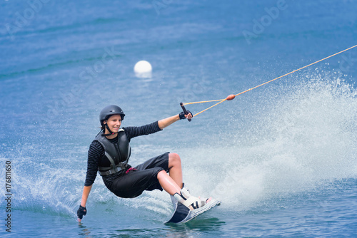 Canvas-taulu Young woman on wakeboard touching water with hand