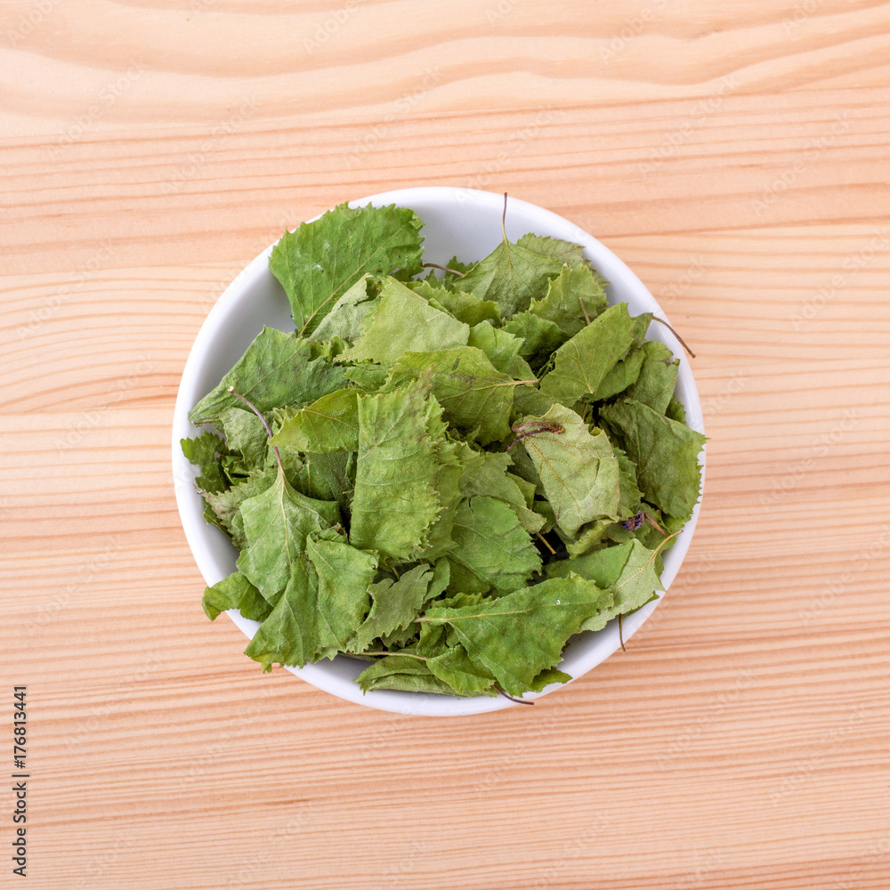 birch leaves / Top view of a porcelain bowl with dried birch leaves on a wooden background birch leaves / Top view of a porcelain bowl with dried birch leaves on a wooden background