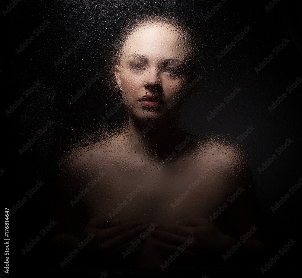 Portrait of a bald girl behind a wet glass on a black background. Portrait of a bald girl behind a wet glass on a black background.