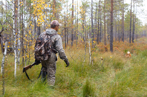 hunter in camouflage with shotgun walking in the forest