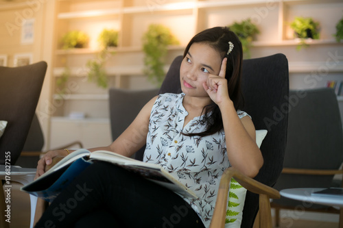 Asian girl reading book in living room with thinking actions.
