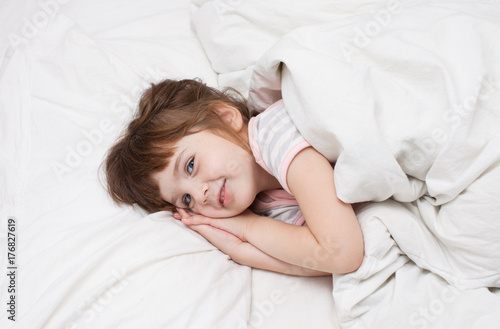 A girl of 4 years smiling in white bed