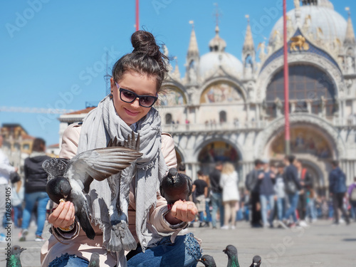 Young female traveler sitting and feeding pigeons on the Piazza San Marco