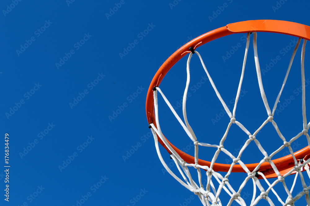 Detail of an orange basketball rim (hoop) and white net against blue sky seen from below Detail of an orange basketball rim (hoop) and white net against blue sky seen from below