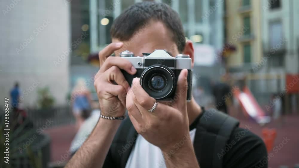 Cute and handsome young man learns how to use and make photographs on vintage retro analog camera, clicks shutter button to make pictures with vintage effect of film Cute and handsome young man learns how to use and make photographs on vintage retro analog camera, clicks shutter button to make pictures with vintage effect of film