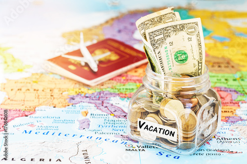 Vacation money savings in a glass jar with passport and aircraft toy on world map, selective focus