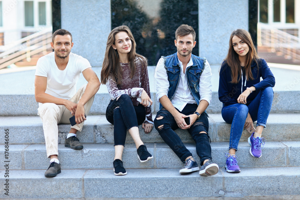 Fototapeta premium Four young people sitting on stairs outdoors with mobile phones
