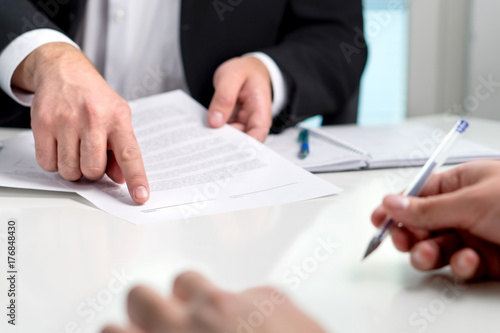 Signing a contract or agreement. Banker or lawyer showing client the line for autograph in a document paper. Business man with a customer in office making deal. Employee hired. photo